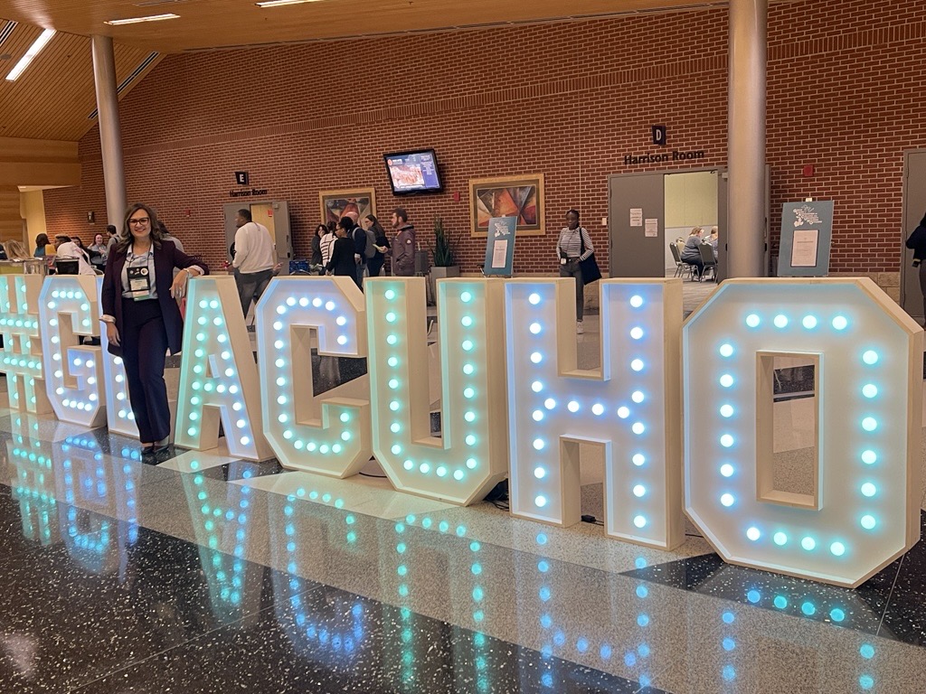 Chief of Staff for REHS Matea Čaluk stands by the conference sign made of lights, spelling out GLACUHO.